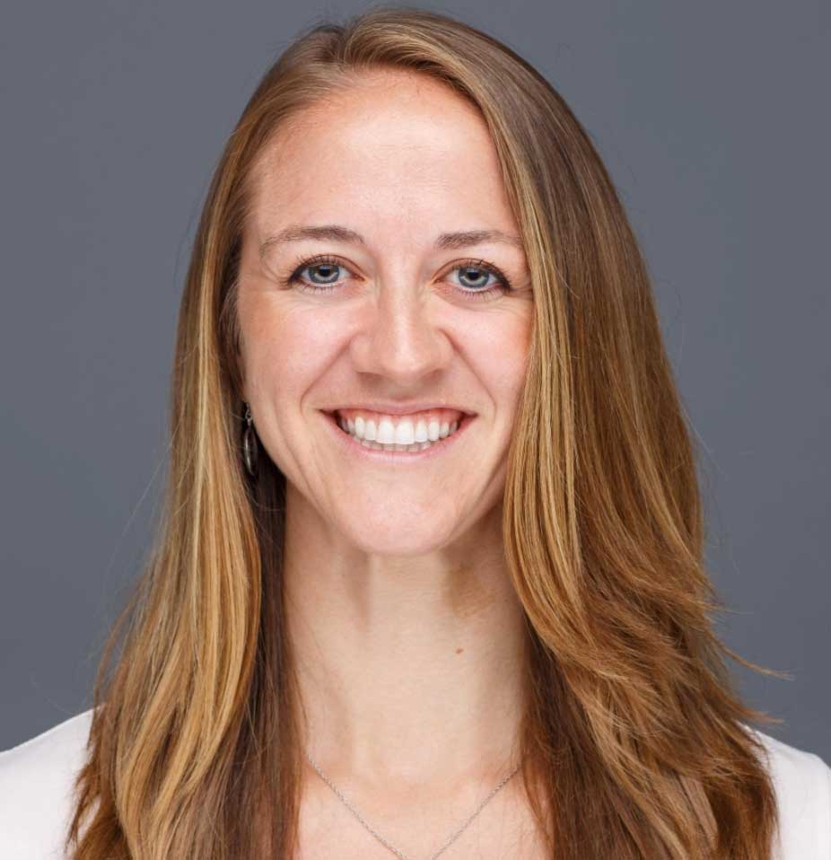 Smiling woman with long, straight, light brown hair against a plain gray background.