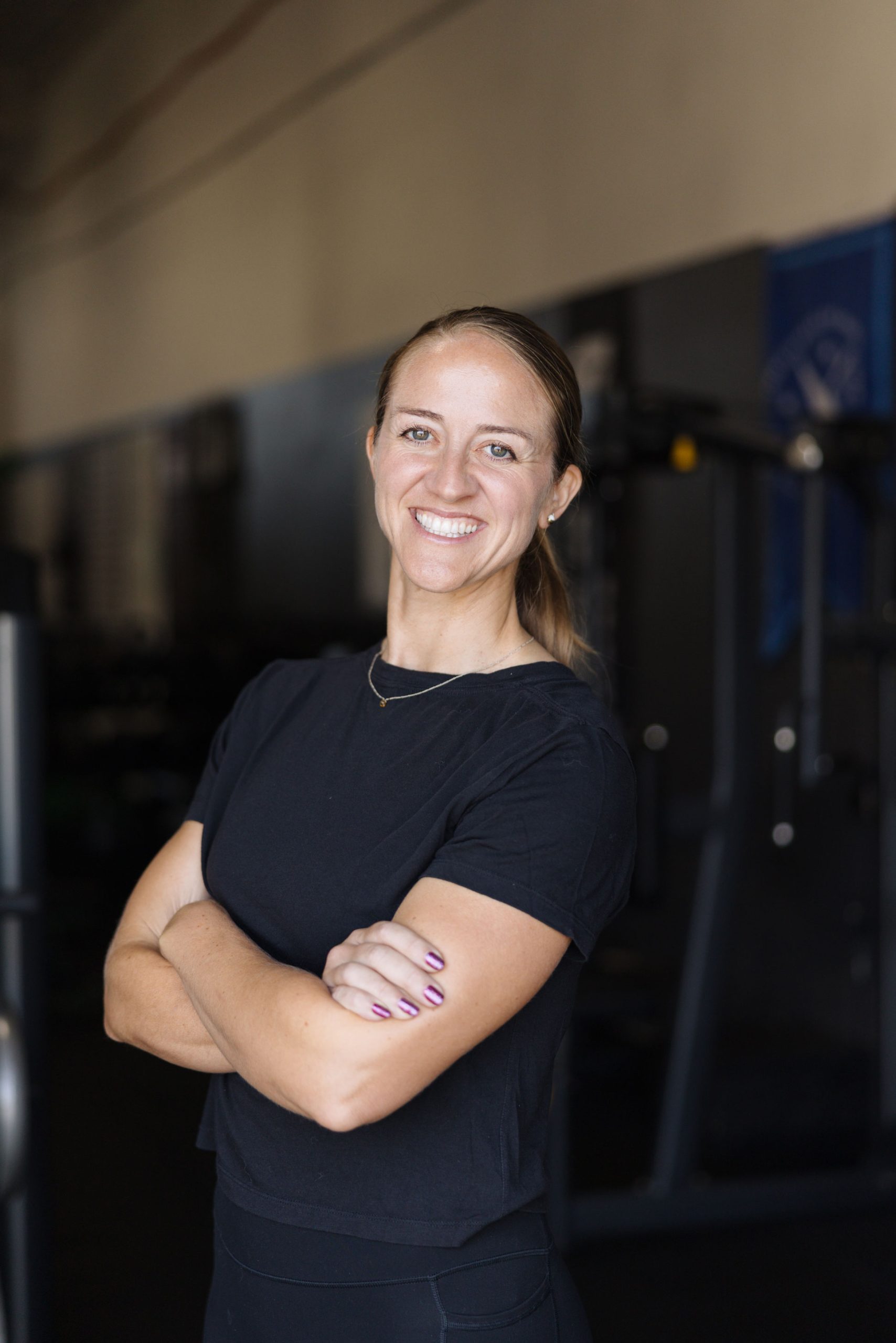 Smiling woman with arms crossed in a gym.